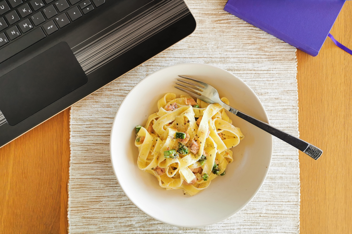 Remote work station with computer, notebook and bowl of pasta