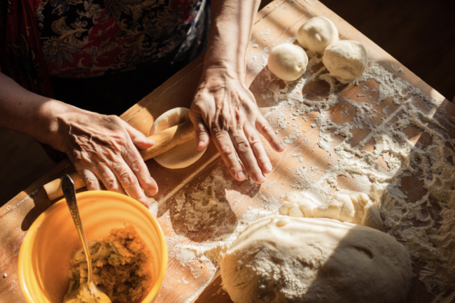 Senior woman hands rolling out dough in flour with rolling pin in her home kitchen