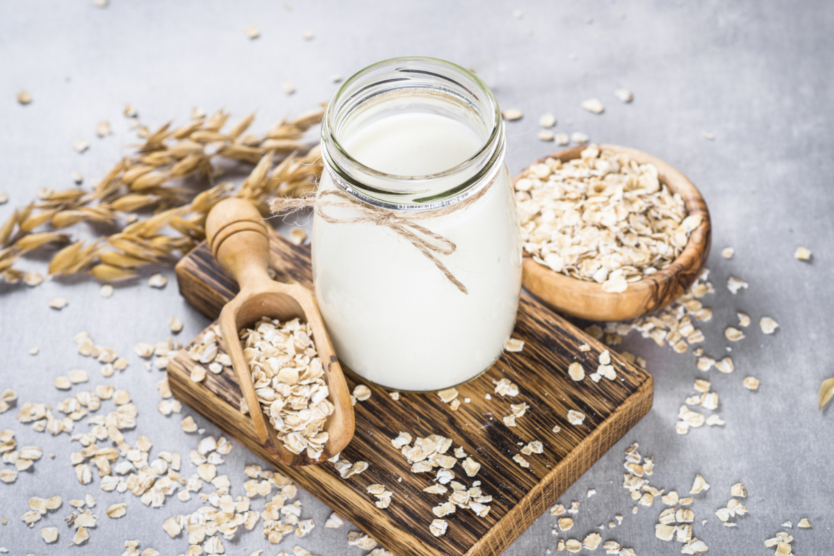 Oat milk on serving tray, glass of milk next to fresh with oats