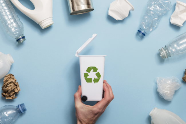 Hand holding a recycling garbage bin with lots of waste packaging