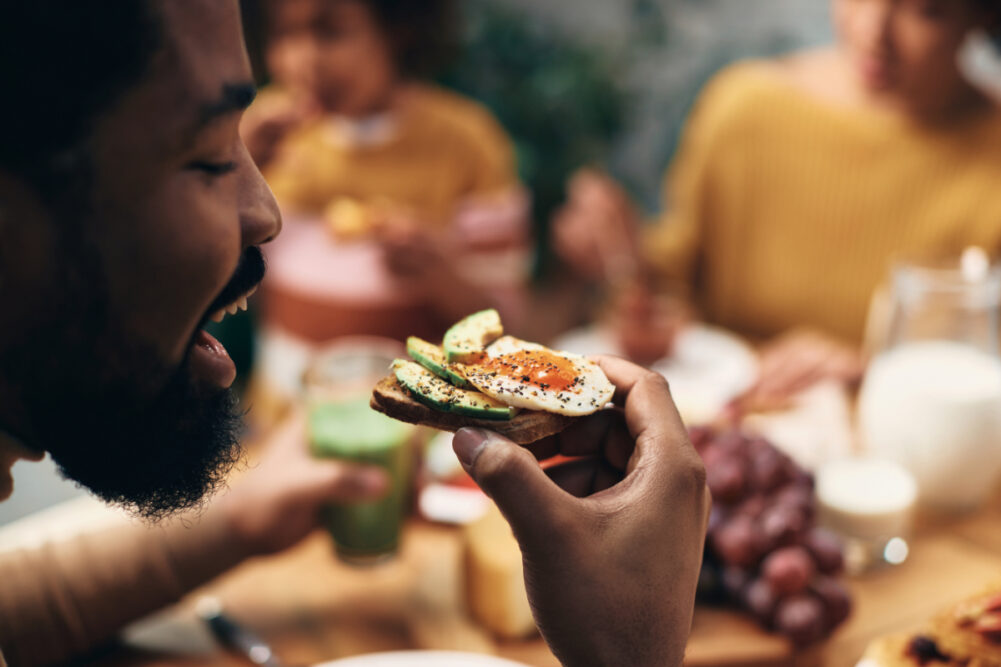 Black man eating avocado toast with his family at home