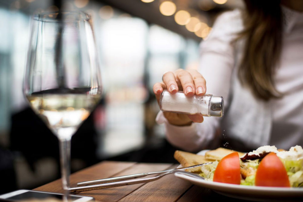 Person sprinkling salt on meal at restaurant