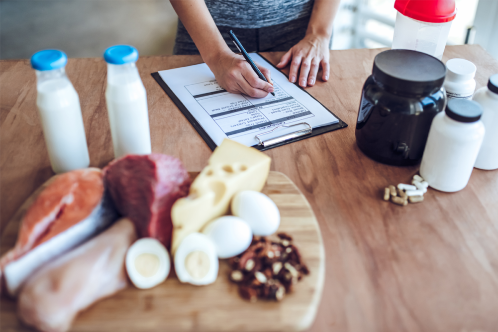 Person writing on a clip board with sports nutrition items