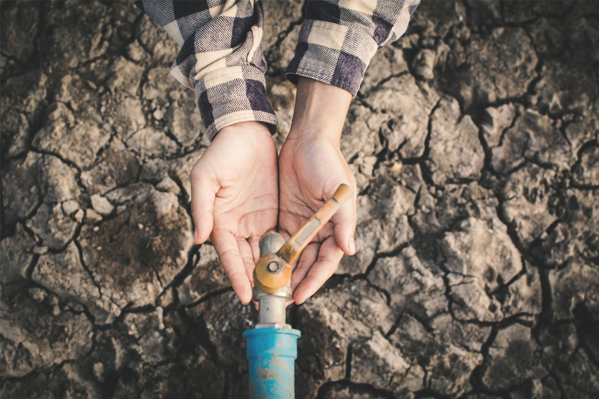 Person trying to get water from a spicket in a drought landscape